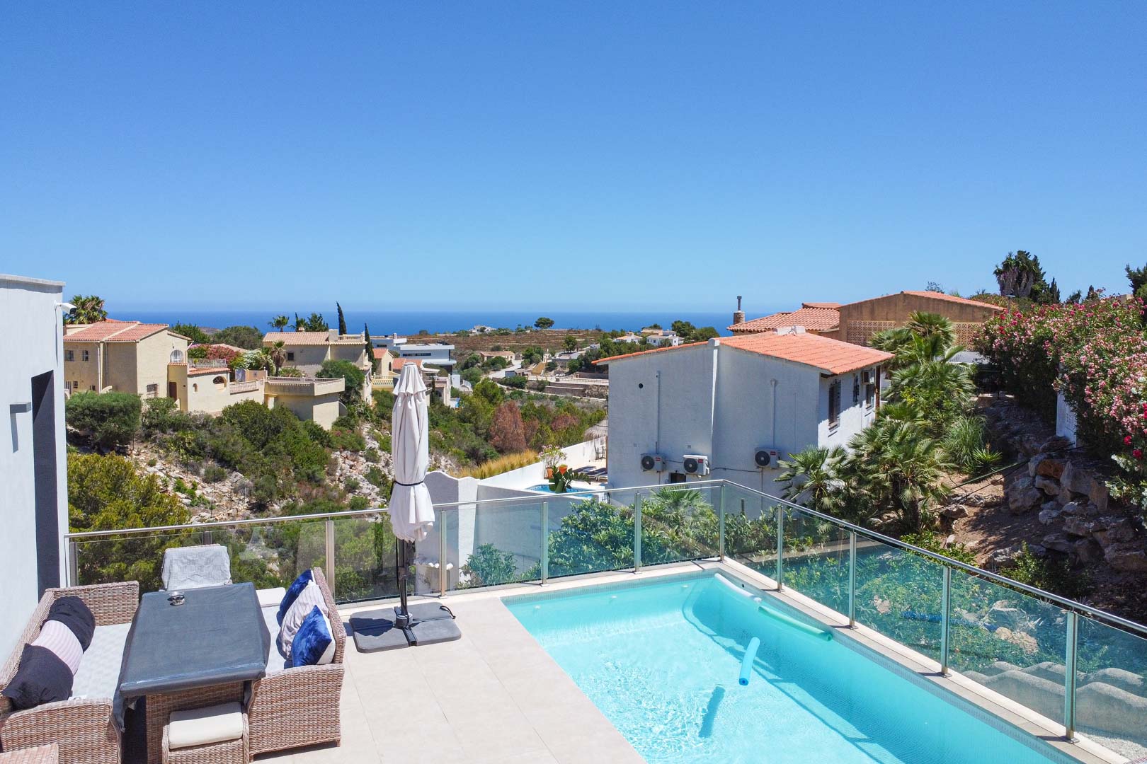 Terraza exterior con piscina, barandilla de cristal y zona de comedor con muebles de mimbre, ofreciendo vistas panorámicas al mar Mediterráneo en Cumbre del Sol.