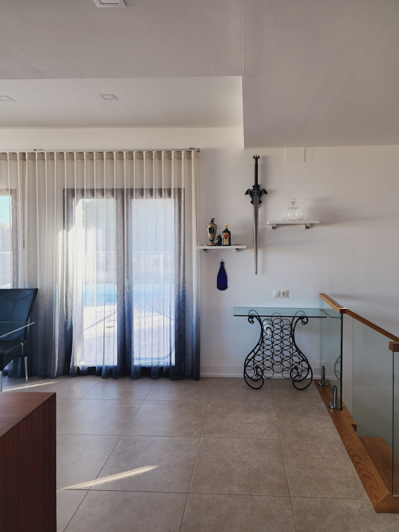 Zona de paso con suelos de gres porcelánico, mesa consola de forja y cristal, y una escalera moderna con barandilla de vidrio y detalles en madera.