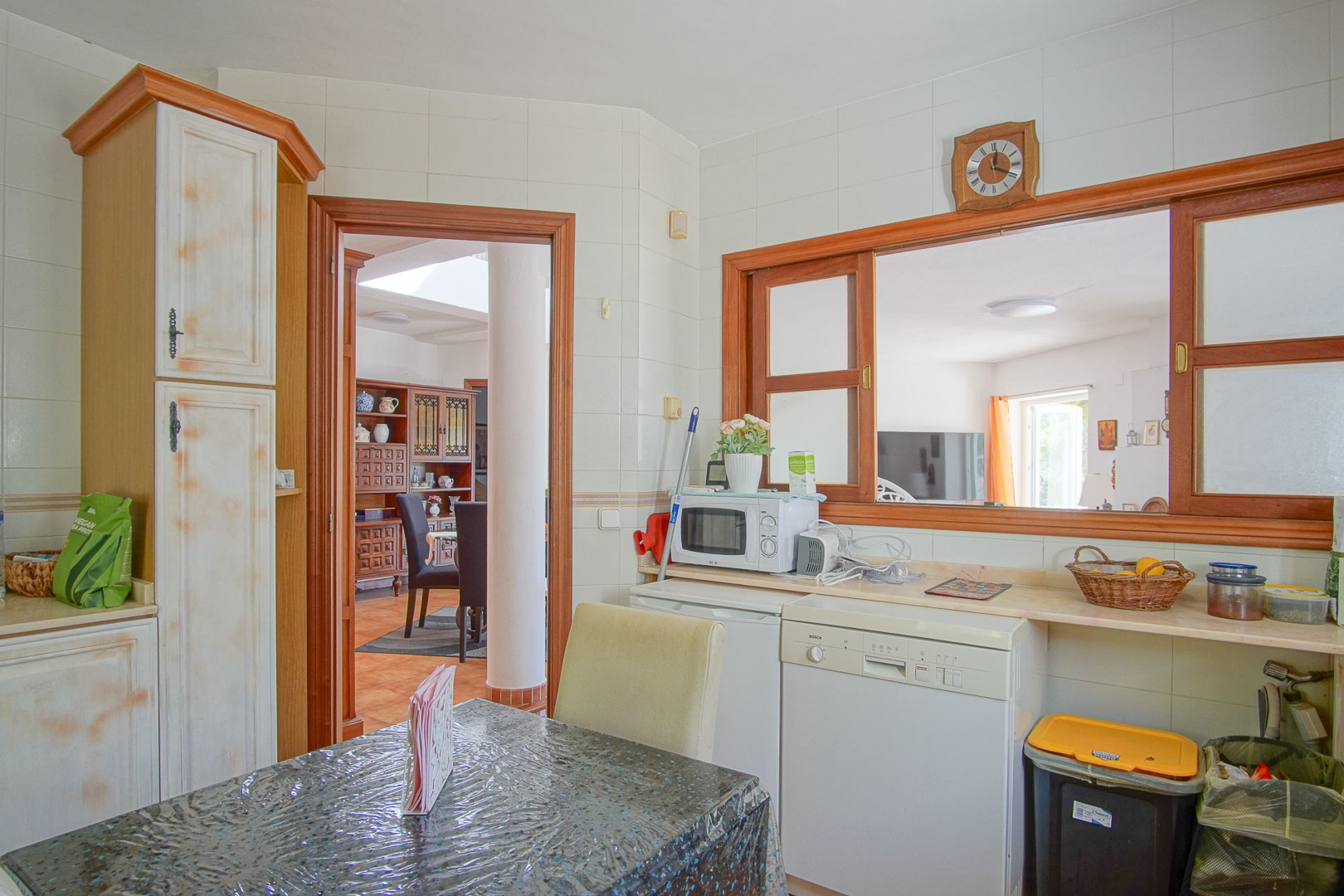 Cocina independiente con mobiliario rústico, zona de desayuno y ventana pasaplatos hacia el comedor. Equipada con lavavajillas y encimera de tono claro.