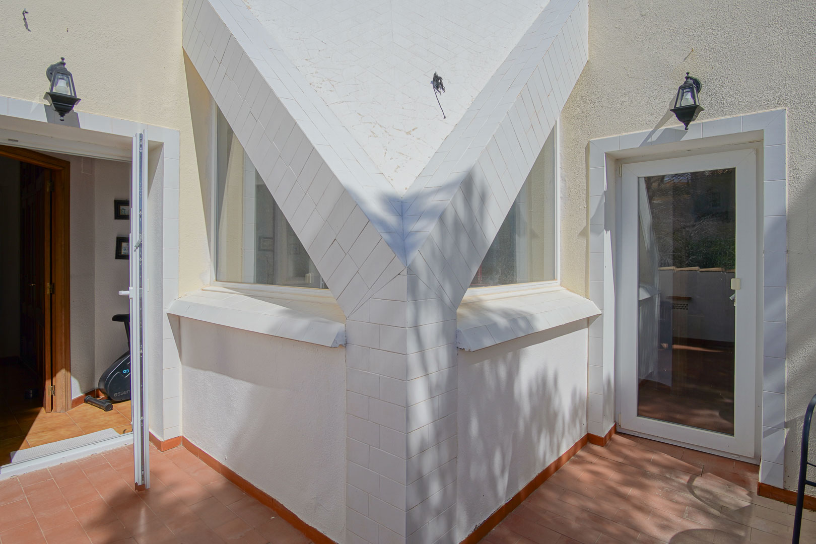 Detalle arquitectónico de la terraza superior con pilares revestidos en azulejo blanco, suelo de terracota y acceso directo a estancias interiores con luz natural.