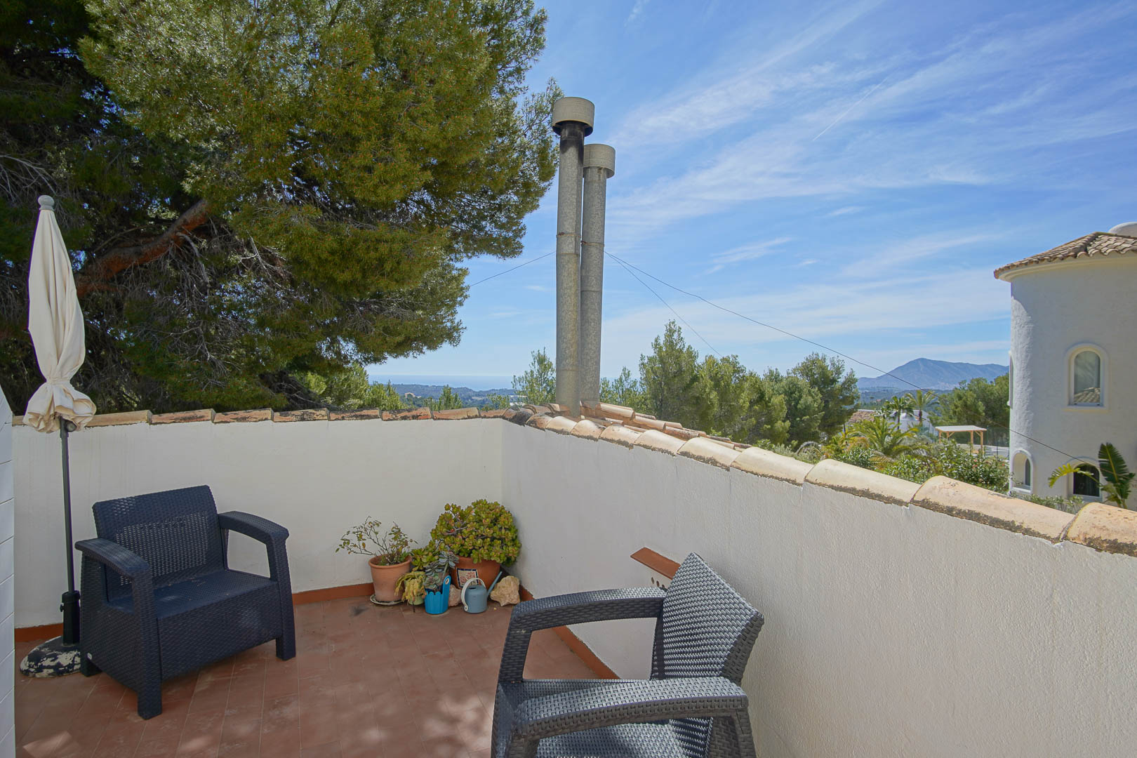 Terraza superior con suelo de terracota y sillones de resina trenzada, ofreciendo vistas despejadas al mar Mediterráneo y al entorno boscoso de Altea.