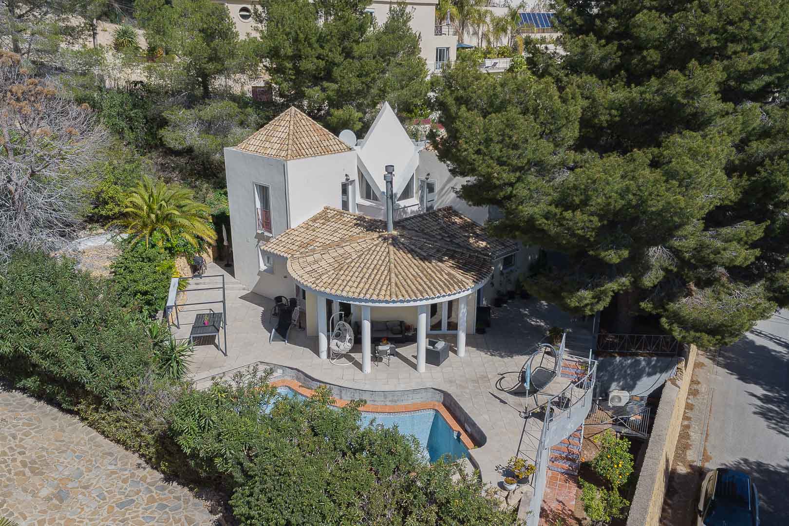 Vista aérea de la villa con su característico porche circular de columnas blancas, piscina privada y amplias terrazas rodeadas de pinos maduros y vegetación.
