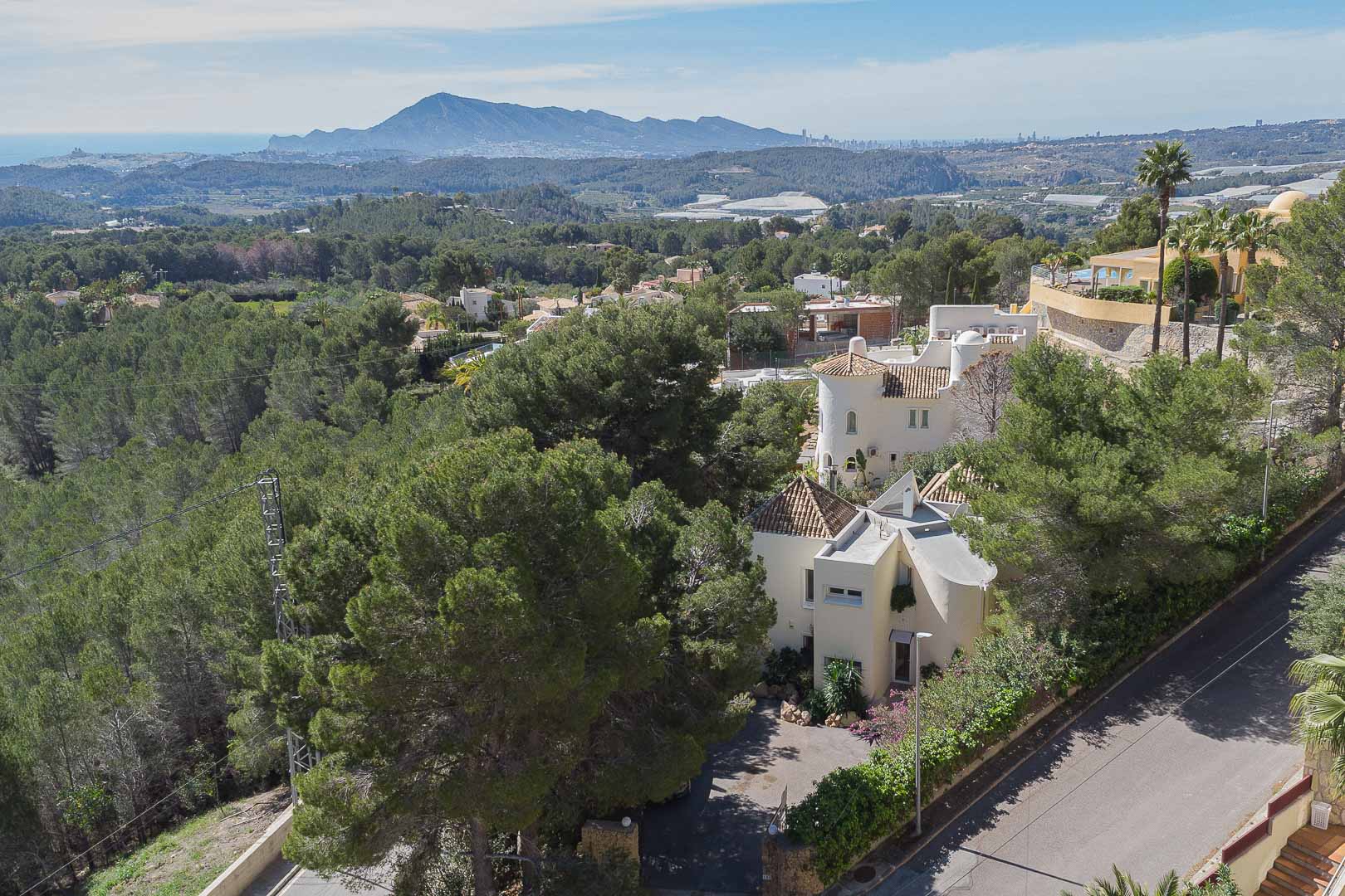 Vista aérea de la villa integrada en la naturaleza, destacando su arquitectura mediterránea y las vistas panorámicas hacia el mar y las montañas de Altea.