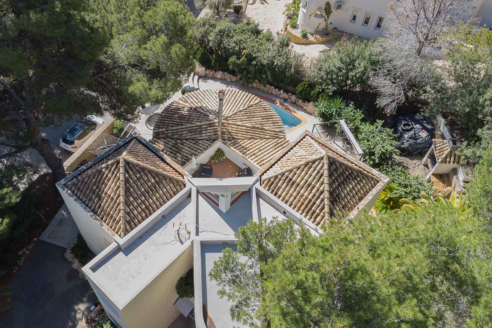 Vista aérea que destaca la arquitectura singular de la villa con cubiertas de teja árabe, chimenea central y una terraza privada integrada entre los volúmenes superiores.