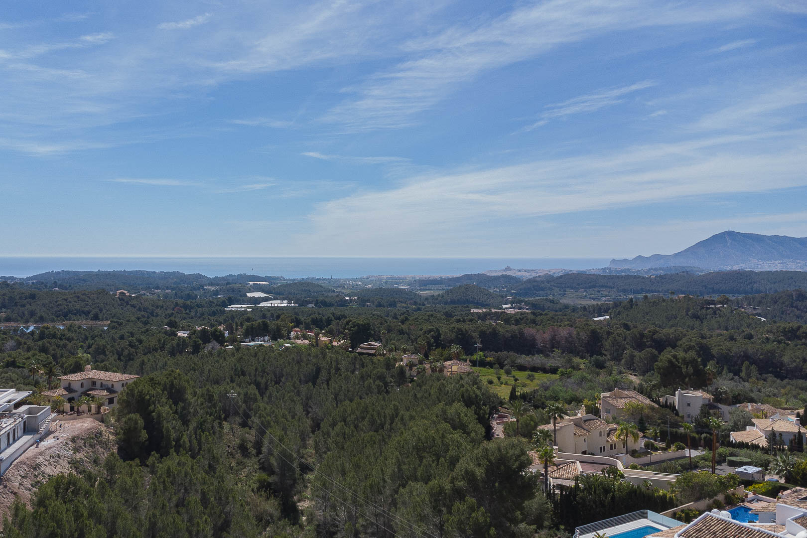 Vista panorámica desde la terraza superior que abarca un frondoso bosque de pinos, el litoral mediterráneo en el horizonte y las siluetas montañosas bajo un cielo despejado.
