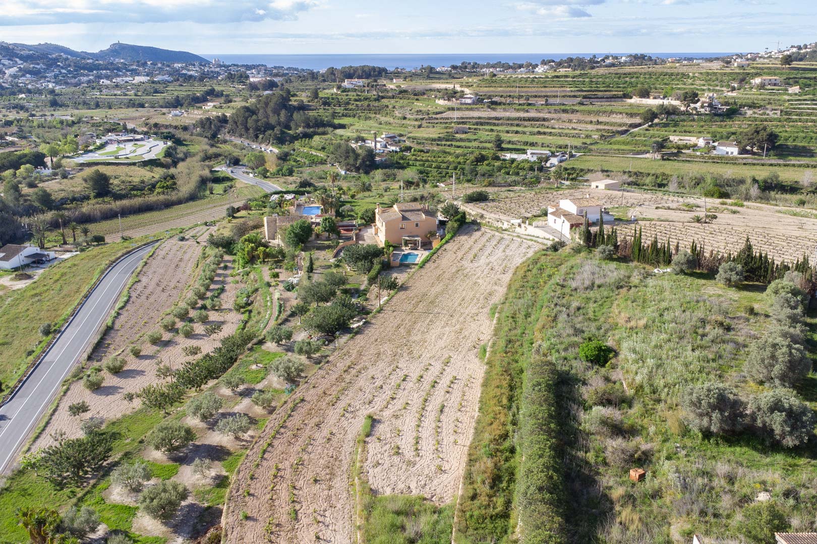 Vista aérea de la amplia parcela de 10.920 m2 en Teulada-Moraira, mostrando el terreno abancalado y las vistas panorámicas hacia la costa mediterránea.