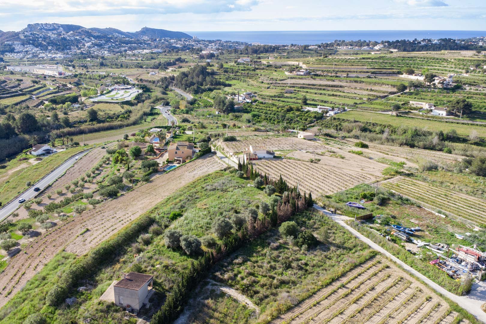 Vista aérea de la amplia parcela rústica de 10.920 m2 en Teulada-Moraira, mostrando su terreno abancalado y vistas despejadas hacia el mar Mediterráneo.
