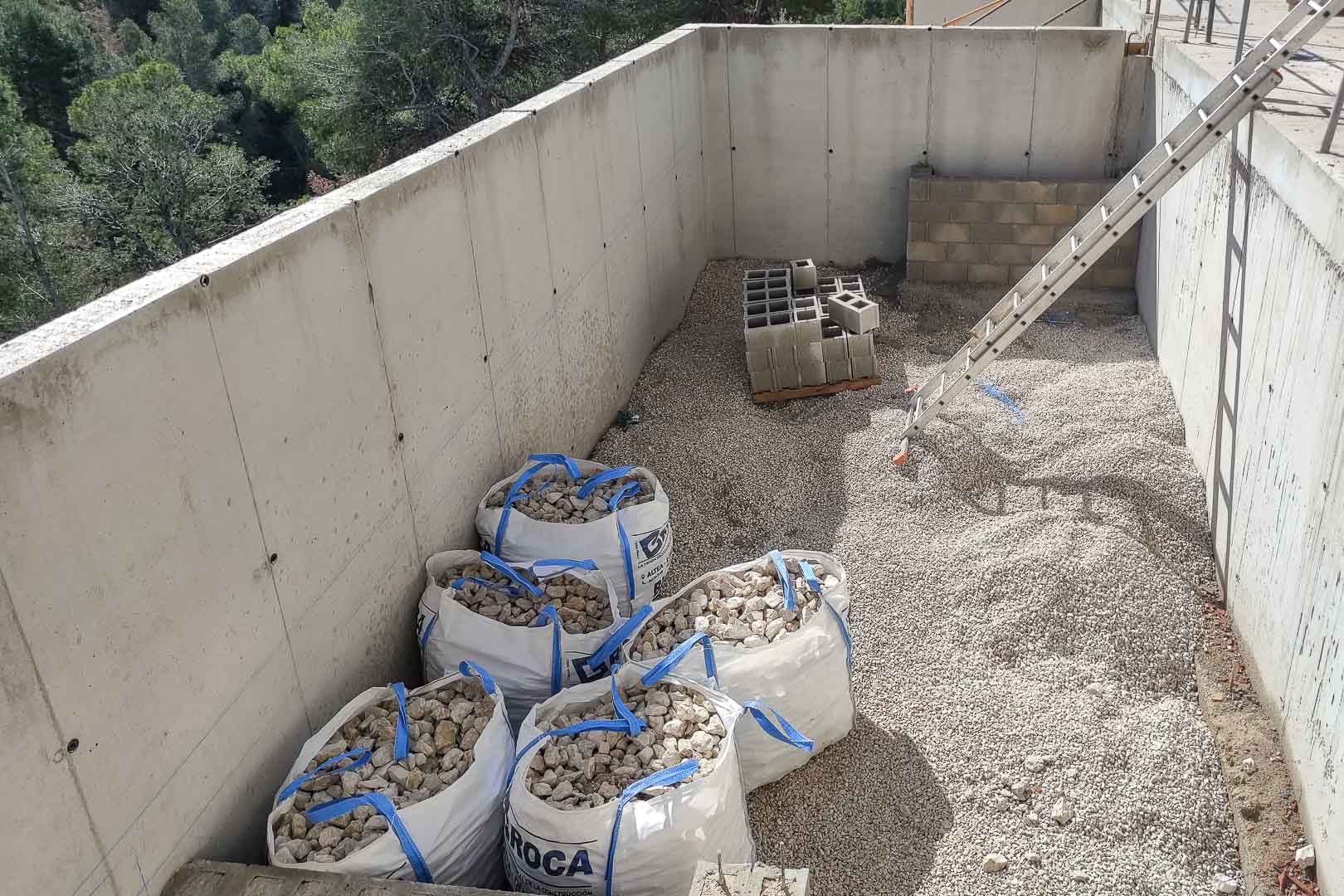 Estado de construcción de la estructura de hormigón armado, con acopio de materiales y muros perimetrales rodeados de la vegetación mediterránea de Altea.