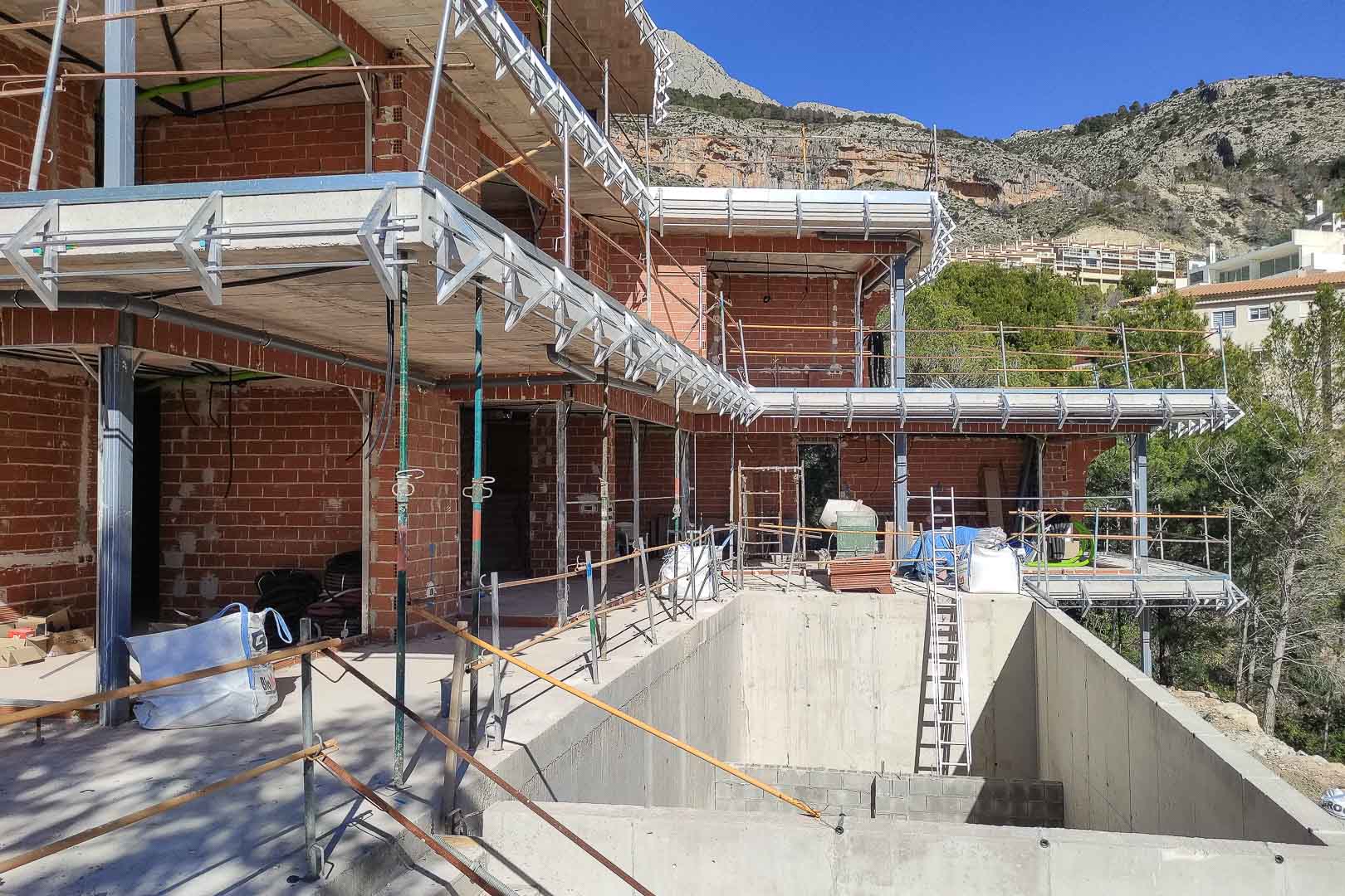 Estado de construcción de la villa en Altea, mostrando la estructura de ladrillo, forjados de hormigón y el vaso de la futura piscina frente a la montaña.