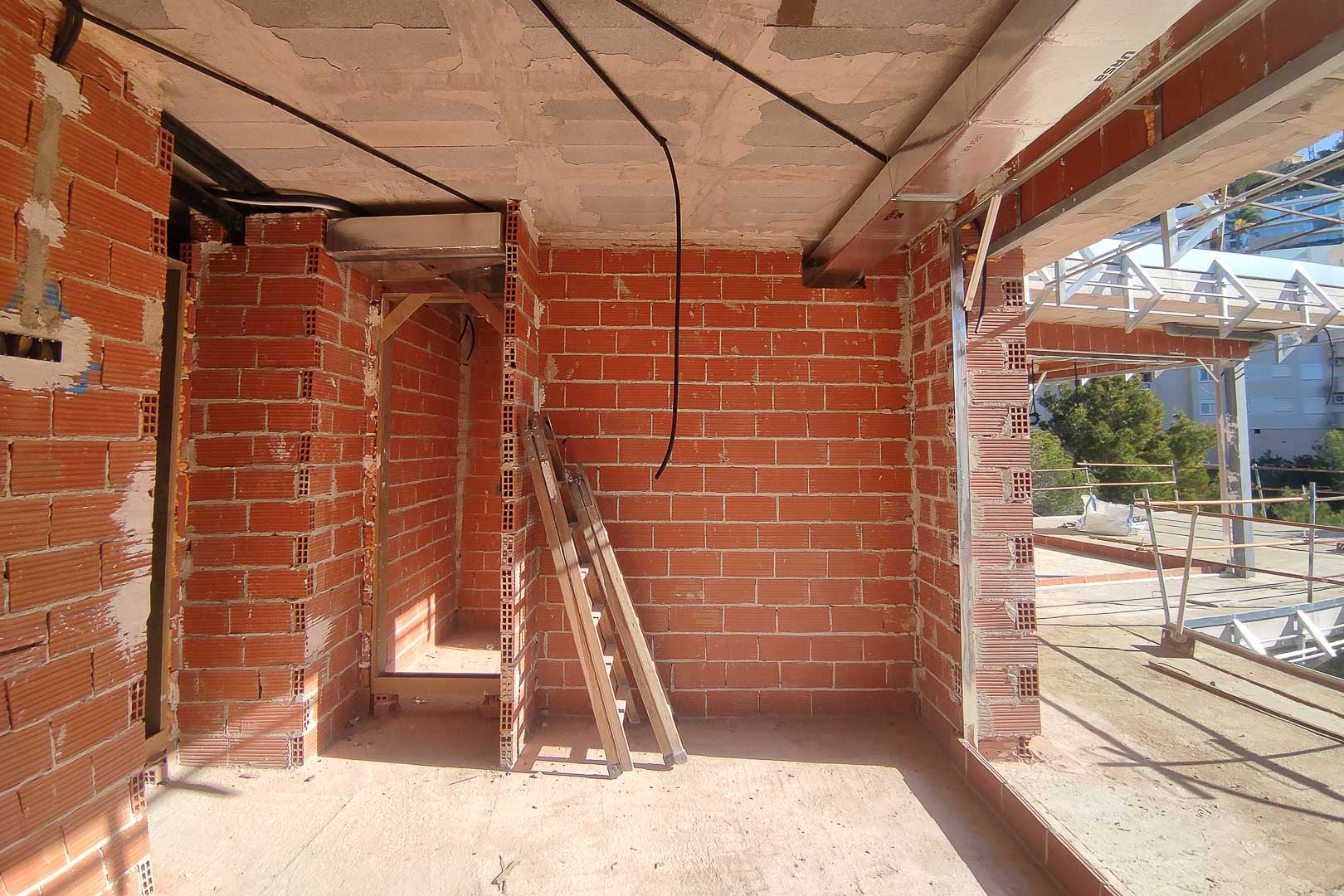 Estado de obra de la villa en Altea mostrando tabiquería de ladrillo, forjados de hormigón e instalaciones de climatización por conductos y cableado.