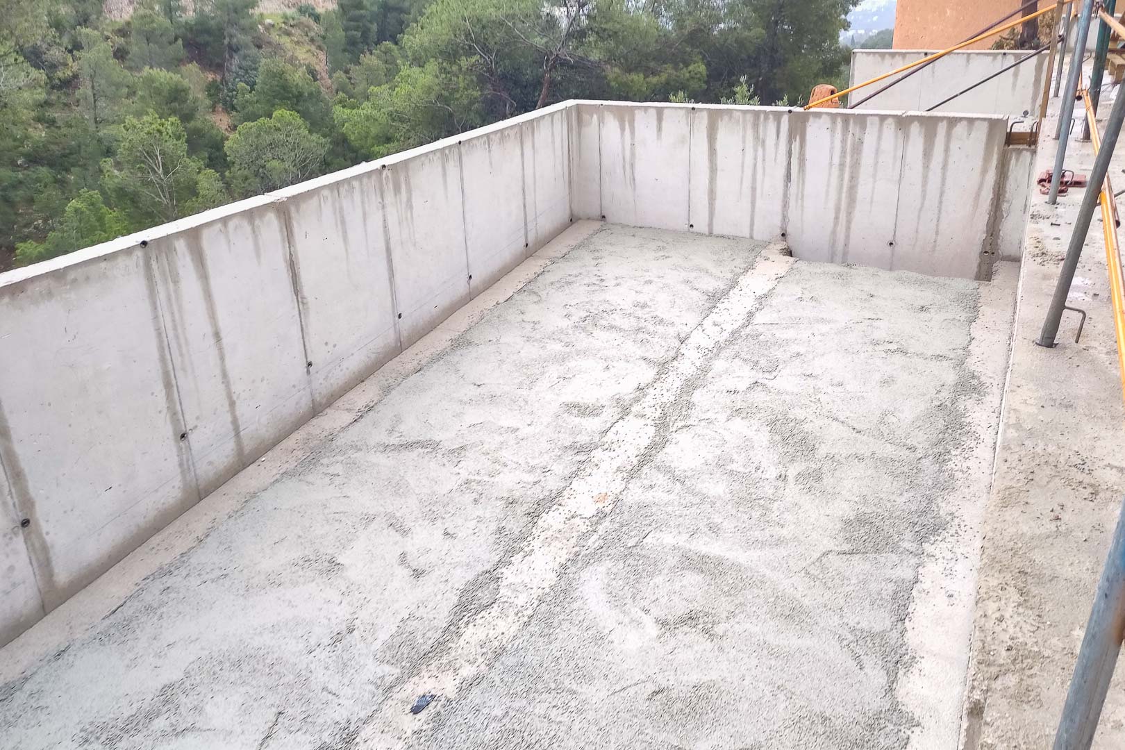 Estructura de hormigón armado en fase de construcción, mostrando los muros perimetrales y el forjado de una futura terraza con vistas al entorno boscoso.