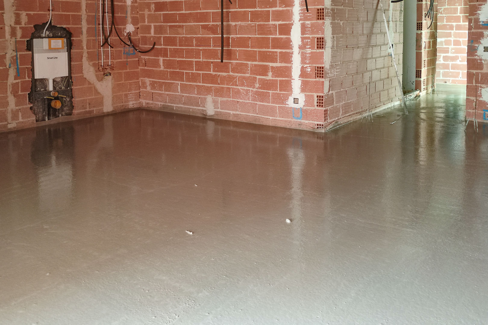 Fase de construcción con mortero autonivelante recién vertido. Se observa la tabiquería de ladrillo y la instalación de cisterna empotrada para sanitario.