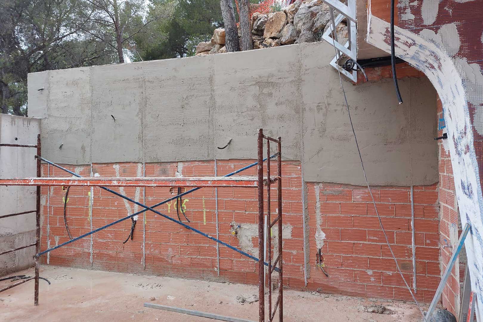 Fase de construcción: enfoscado de muros perimetrales de ladrillo con preinstalación eléctrica y andamiaje técnico en la estructura exterior.