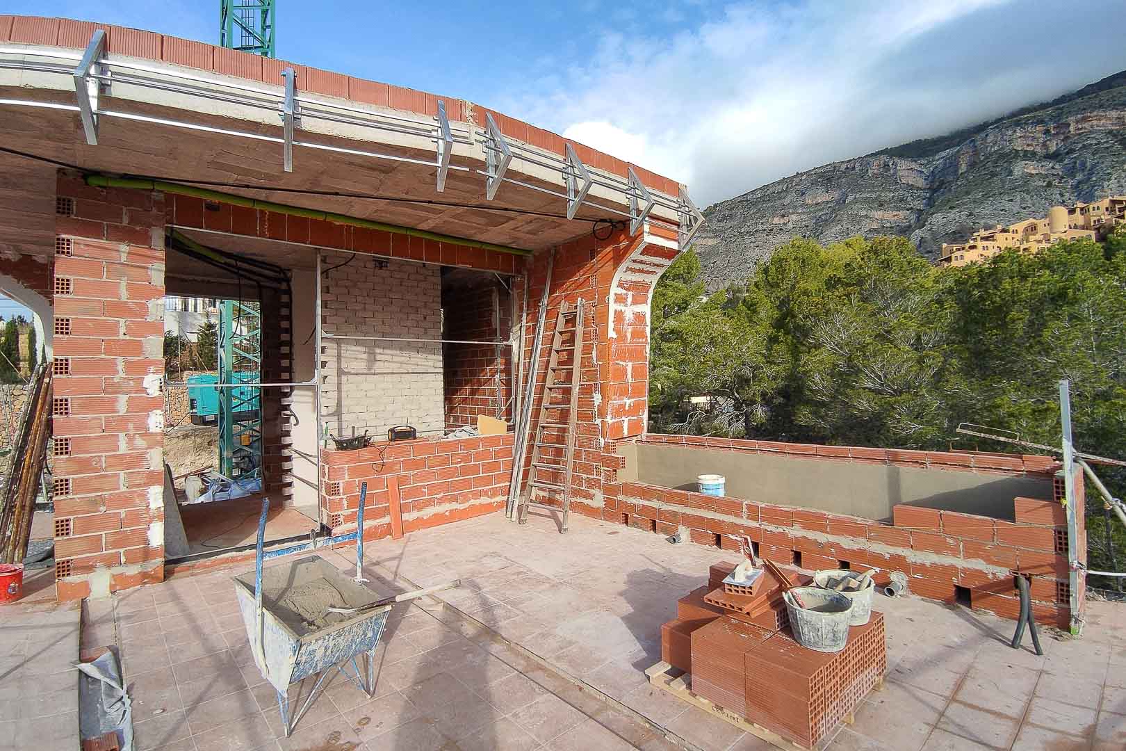 Vista de la fase de construcción de la terraza superior, mostrando la estructura de ladrillo, forjados de hormigón y soportes metálicos exteriores con vistas a la montaña.