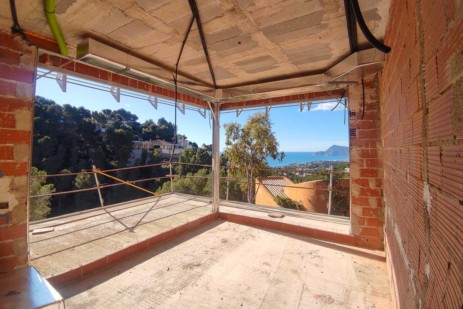 Vista panorámica al mar y la montaña desde una estancia en construcción con grandes ventanales de esquina y conductos de climatización vistos.