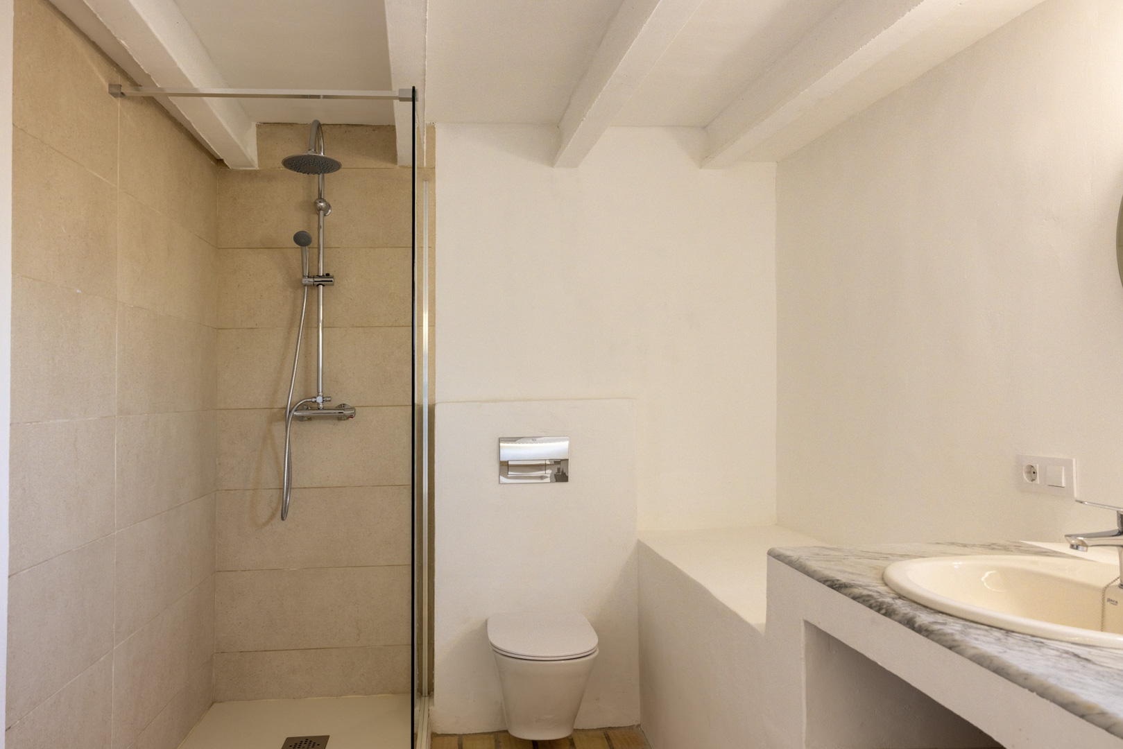 Cuarto de baño con ducha de pared de azulejos color crema, inodoro blanco y lavabo con encimera de mármol.