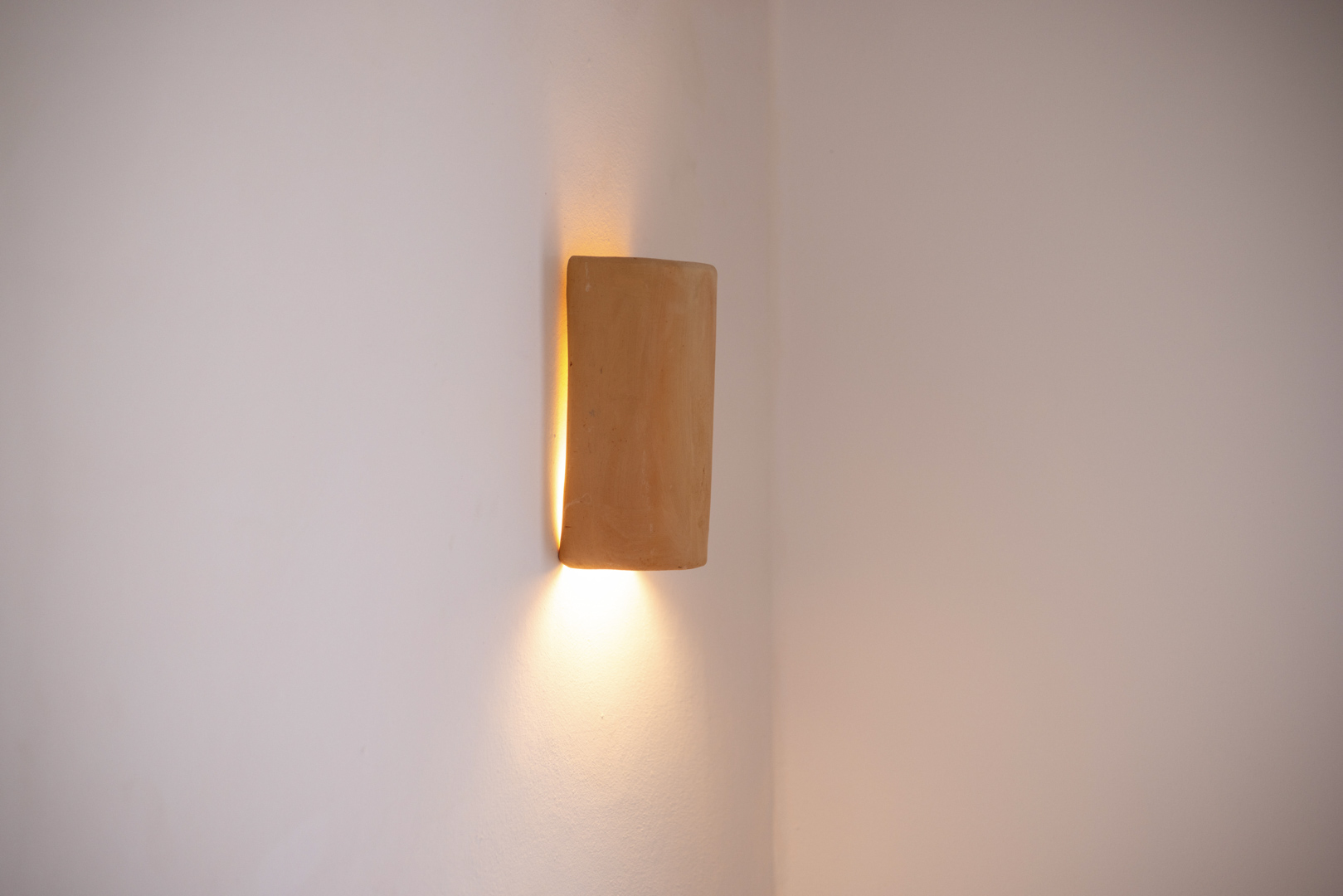 Detalle de aplique de pared rústico, emitiendo luz cálida en un interior minimalista.