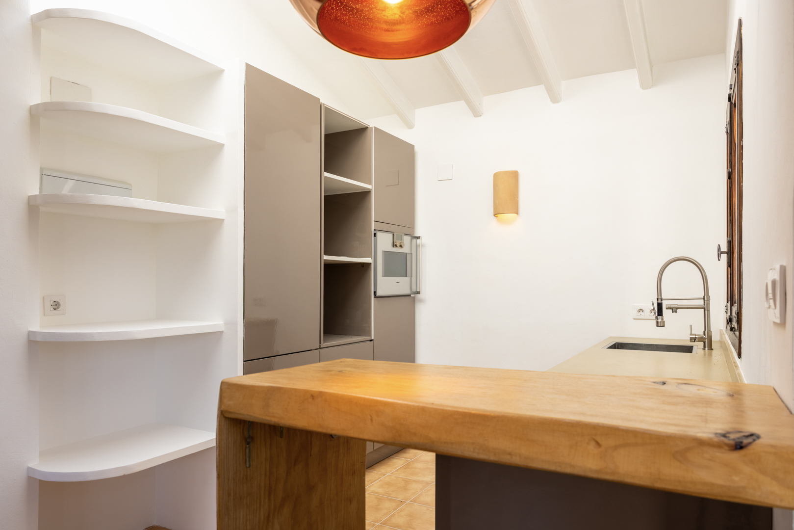 Detalle de cocina con isla de madera, estanterías blancas y luz cálida.