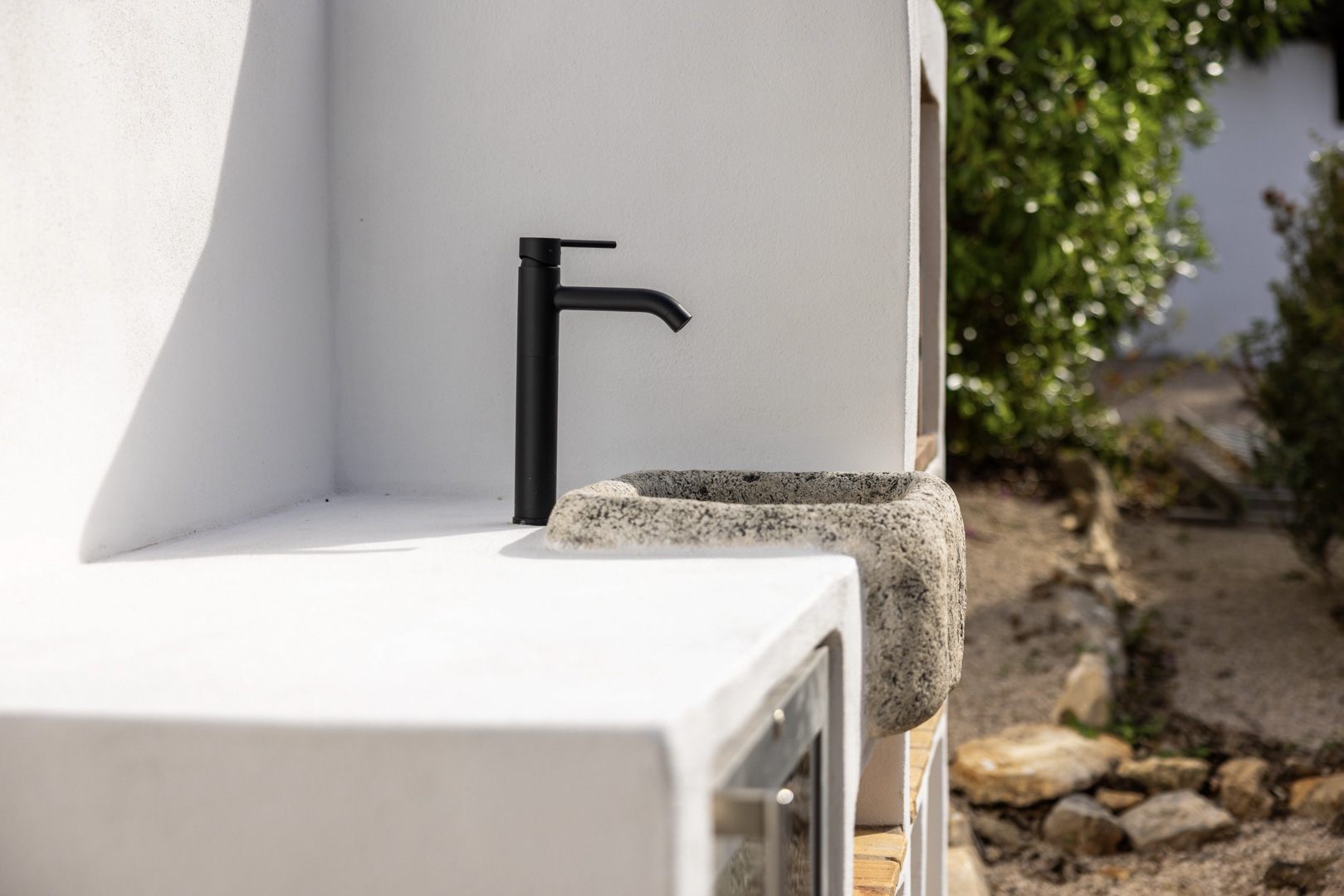 Detalle de la cocina exterior: pila rústica de piedra con grifo negro sobre encimera blanca.