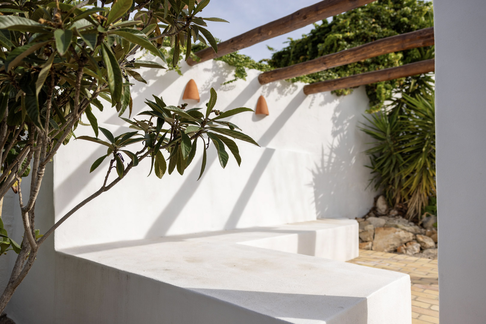 Detalle de la terraza con banco de obra encalado, pérgola de madera y vegetación exuberante.