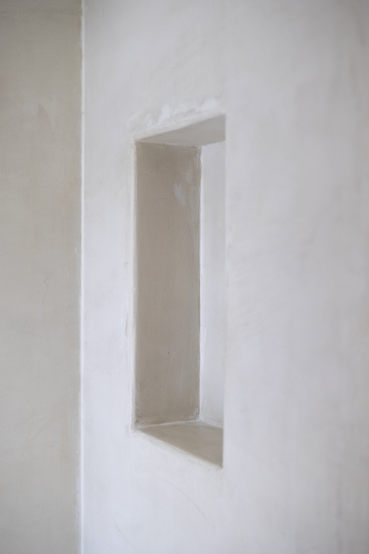 Detalle de nicho rectangular en pared blanca con textura suave. Iluminación natural.
