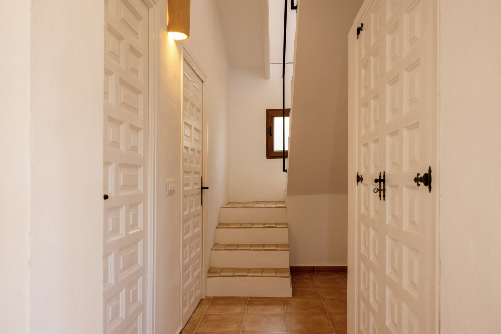 Detalle del vestíbulo con escalera de baldosa y puertas de madera blanca con diseño geométrico.