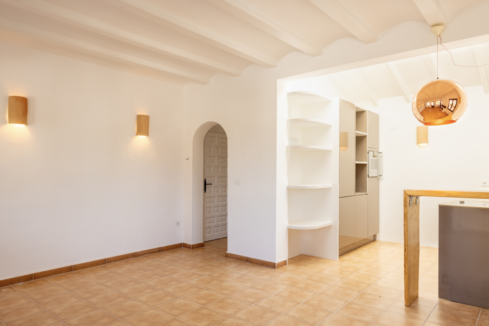 Interior luminoso con estanterías blancas y cocina abierta. Lámpara colgante esférica cobriza.