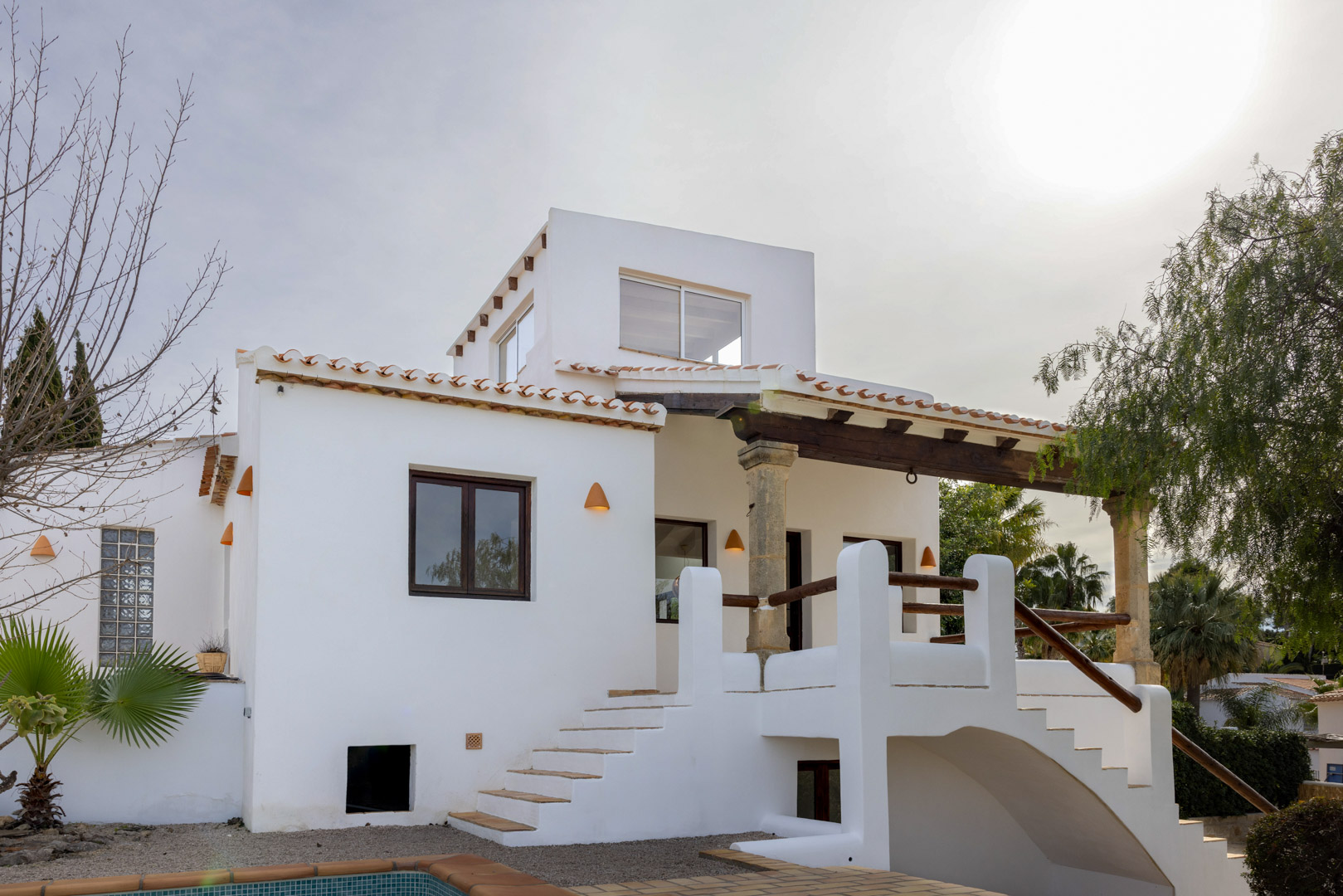 Vista exterior de la villa mostrando la entrada principal con escalera de acceso y detalles arquitectónicos mediterráneos.