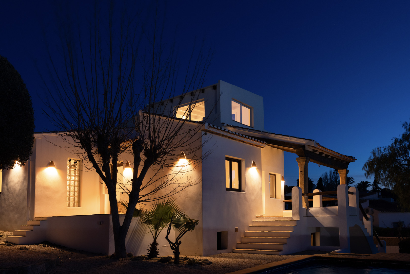 Vista nocturna de la villa con fachada blanca iluminada y detalles de piedra en el porche.