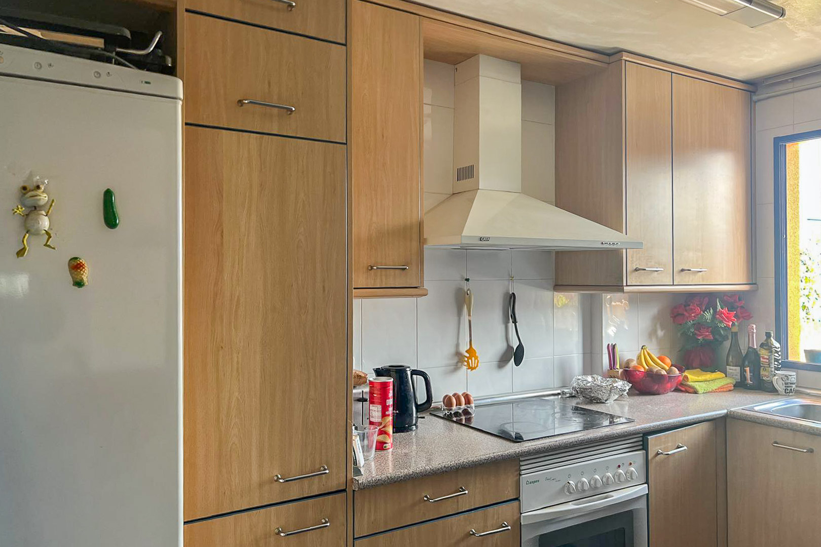 Cocina funcional con armarios de madera clara, electrodomésticos blancos y encimera de granito.