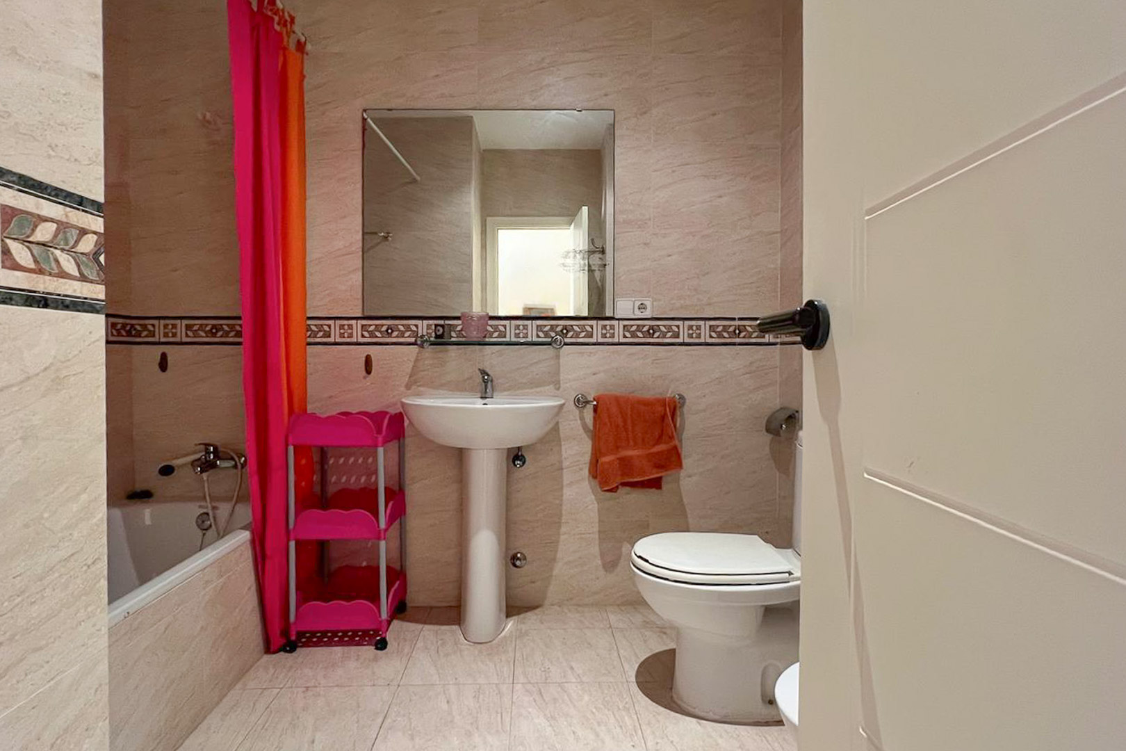 Cuarto de baño con azulejos color crema, lavabo de pedestal blanco y detalles decorativos en la pared.