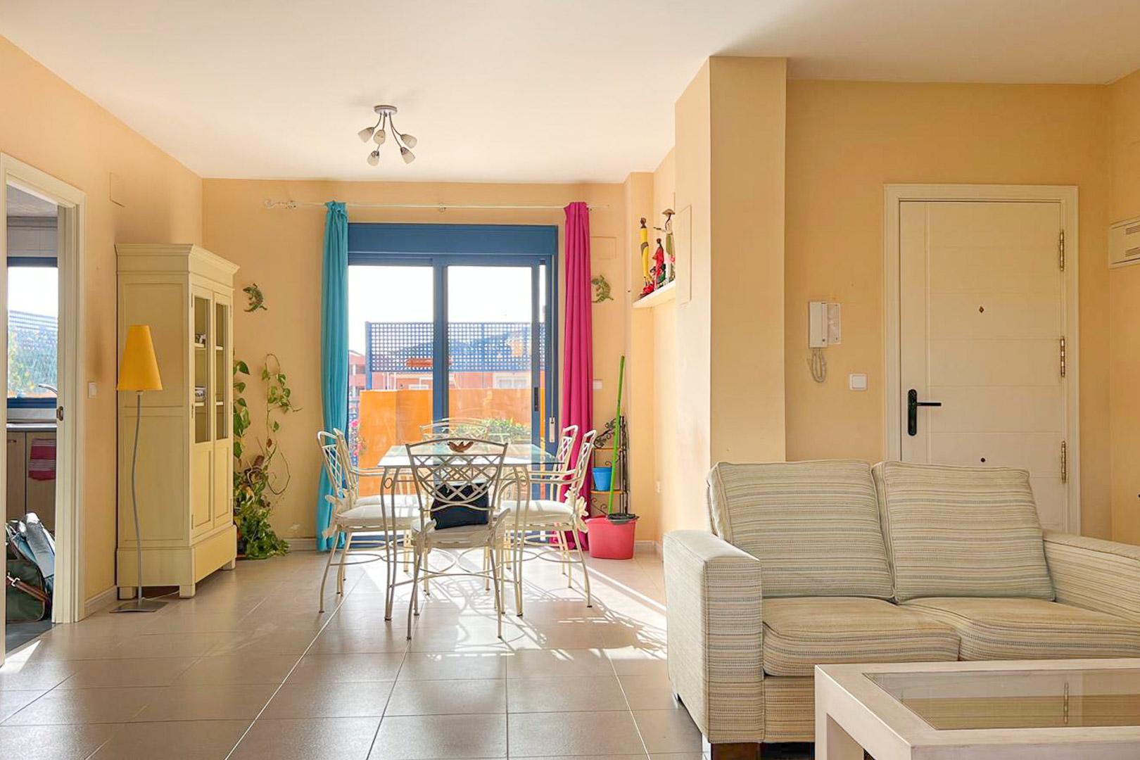 Luminoso salón-comedor con balcón, mesa de comedor metálica y sofá a rayas en tonos neutros.