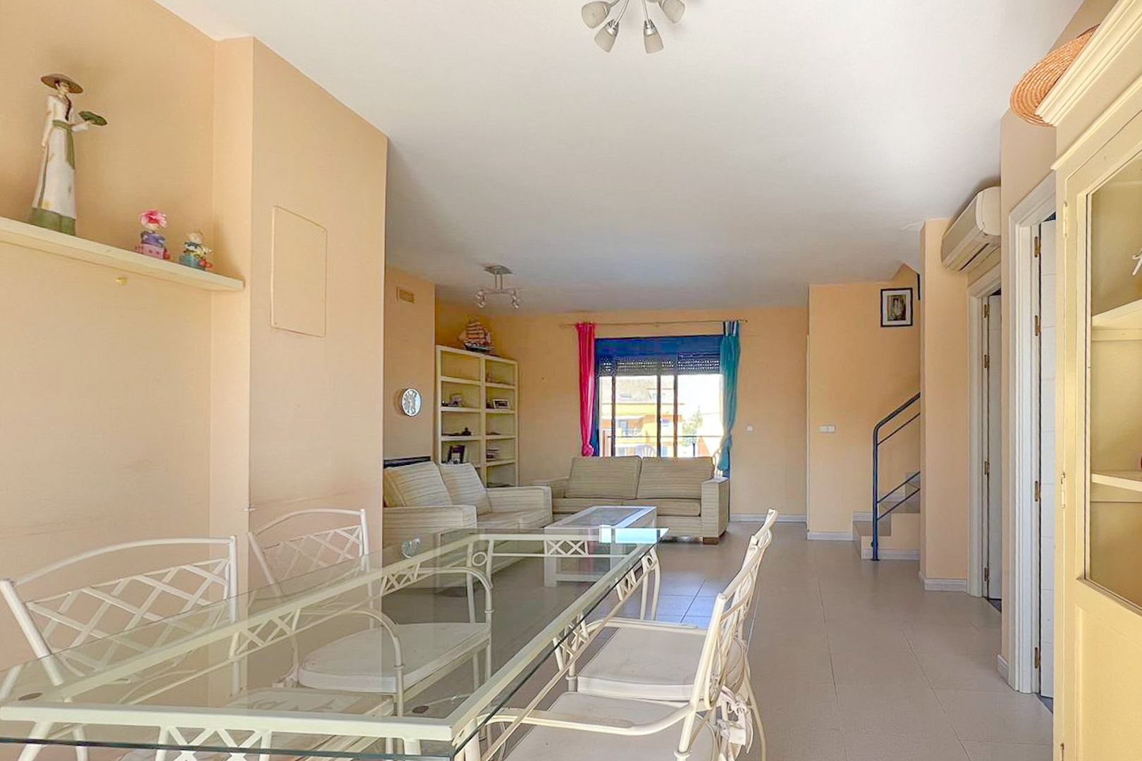 Salón comedor con mesa de cristal, sofás a rayas y estantería con decoración náutica.