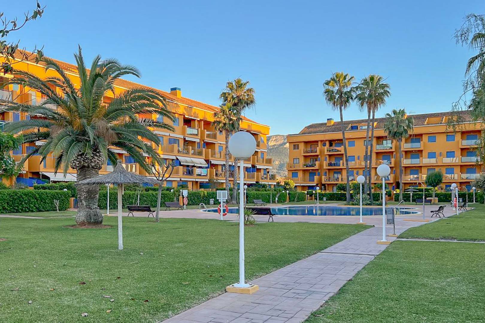 Vista del jardín comunitario con piscina, palmeras y edificios residenciales en Dénia.