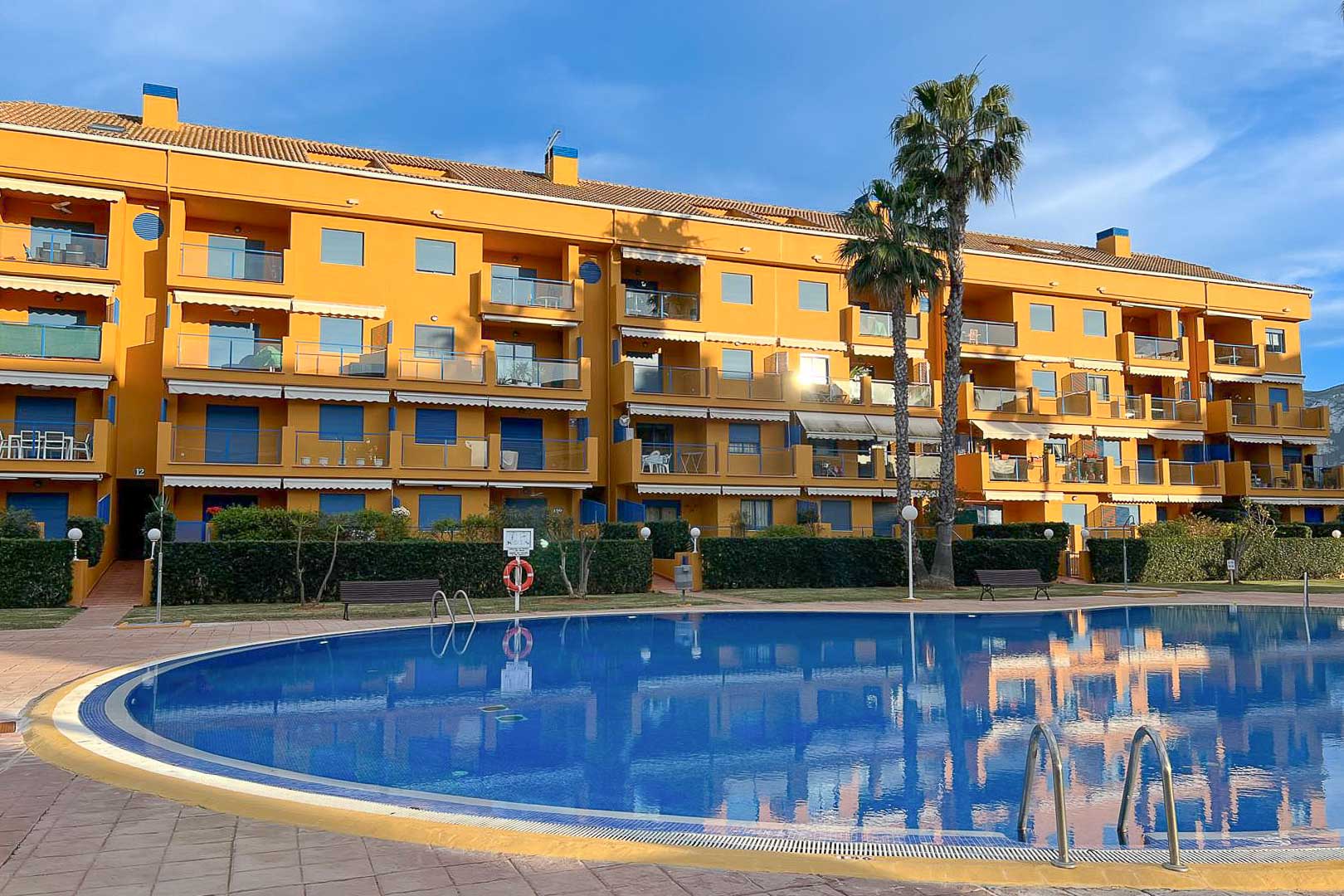 Vista exterior de la piscina comunitaria y fachada del edificio residencial en Dénia.