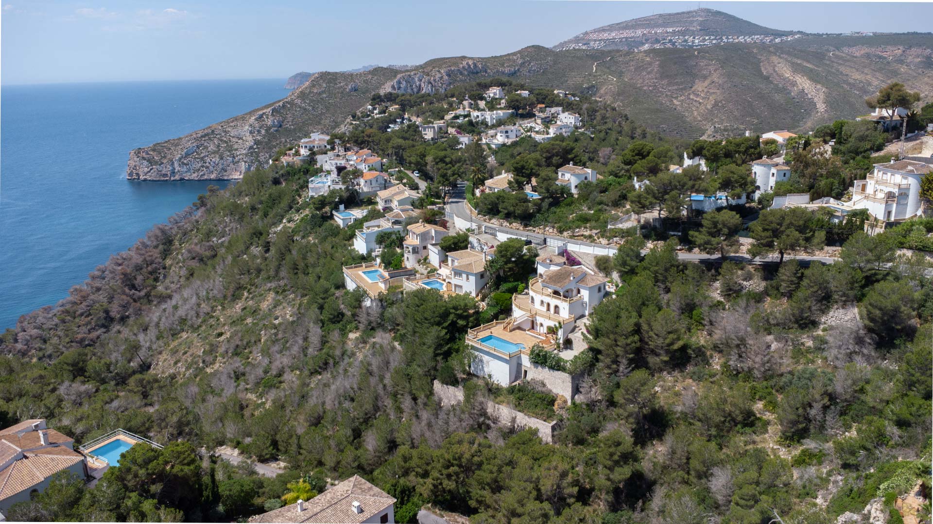 Vista aérea de la costa de Jávea con villas residenciales integradas en la ladera boscosa frente al mar Mediterráneo y los acantilados de la zona.