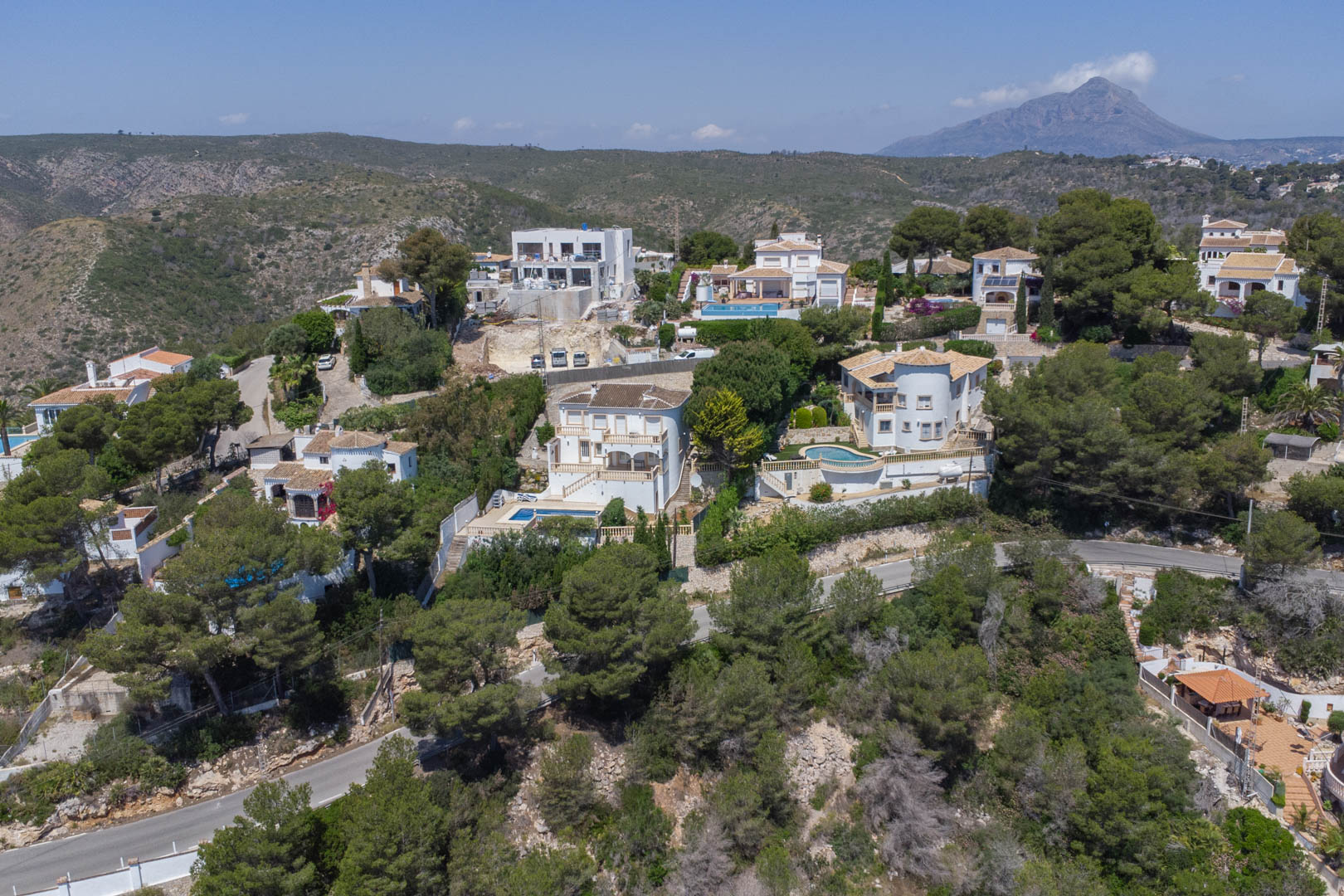 Vista aérea de la urbanización Costa Nova en Jávea, mostrando villas de estilo mediterráneo rodeadas de pinos y el monte Montgó al fondo.