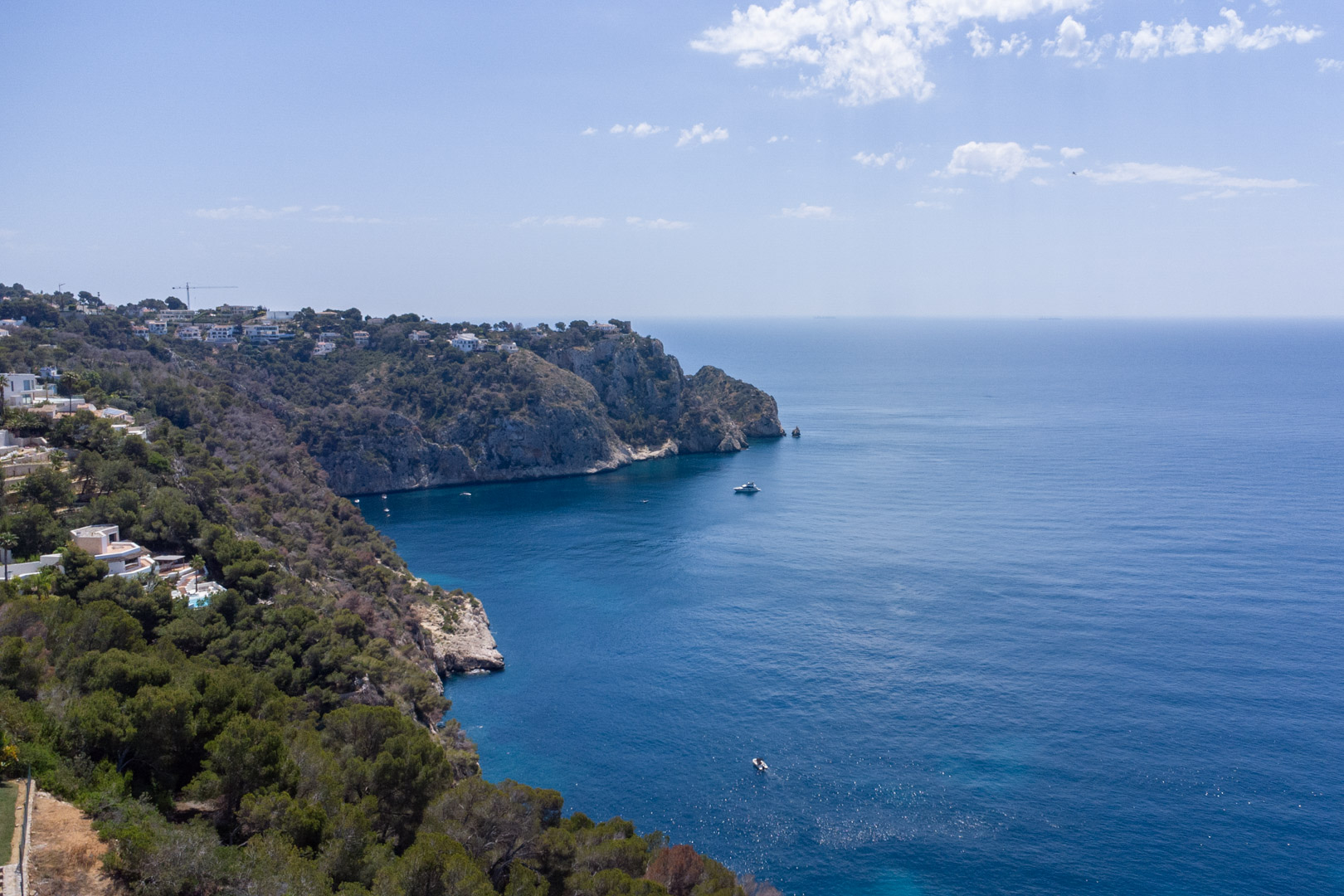 Vista aérea de los acantilados de la Granadella en Jávea, mostrando la costa escarpada con pinos mediterráneos y el mar azul profundo bajo un cielo despejado.