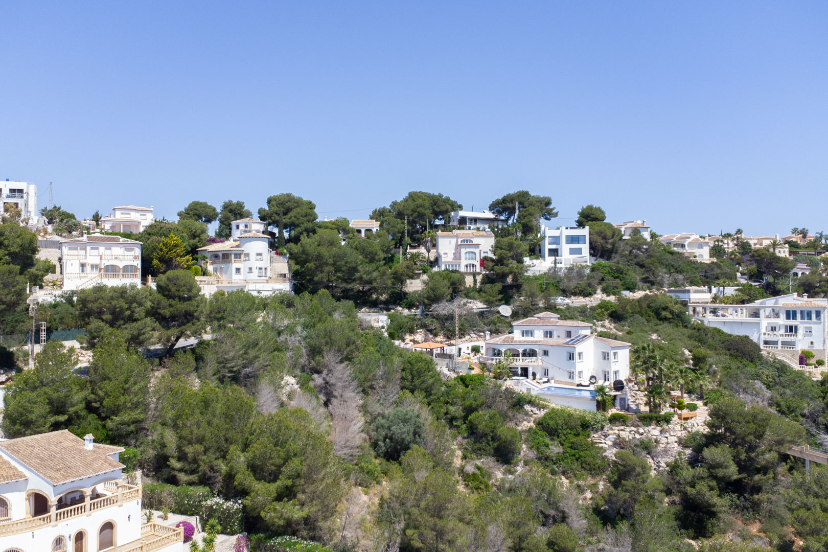 Vista elevada de la urbanización Costa Nova en Jávea, mostrando villas blancas integradas en la ladera boscosa bajo un cielo despejado.