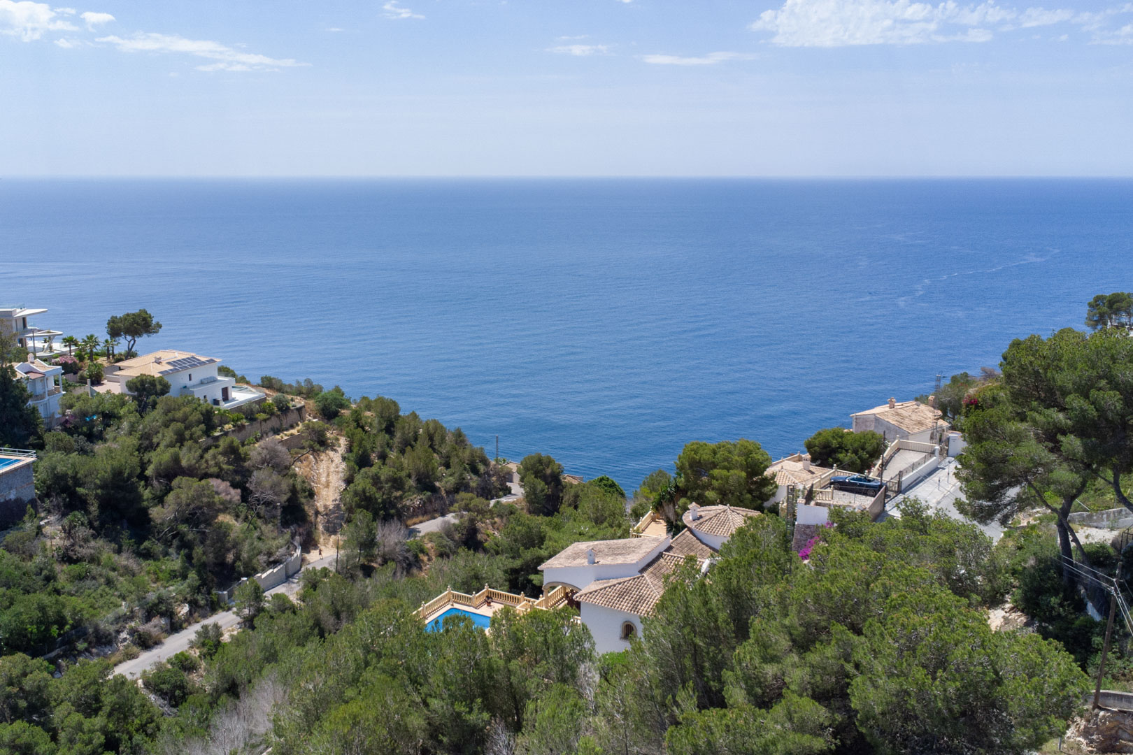 Vista aérea de la costa de Jávea con el mar Mediterráneo en el horizonte, rodeada de pinos y villas tradicionales en la zona de Costa Nova.
