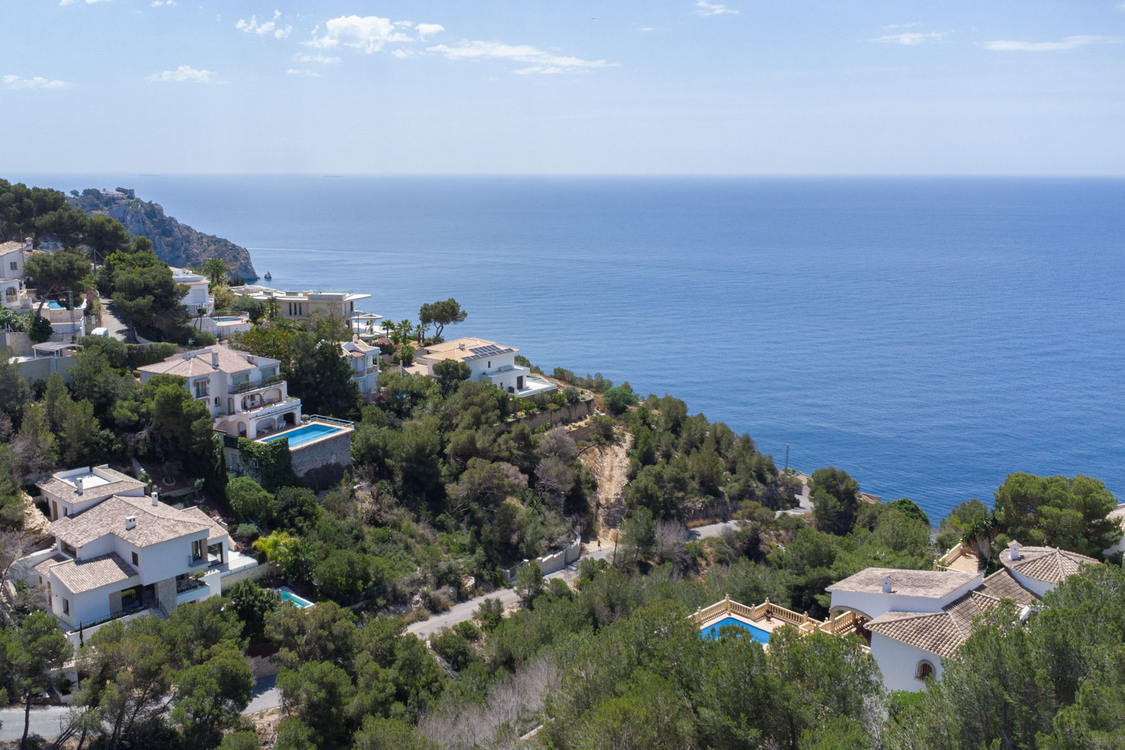Vista aérea de la costa de Jávea con villas de estilo mediterráneo rodeadas de vegetación autóctona y amplias vistas al mar Mediterráneo.