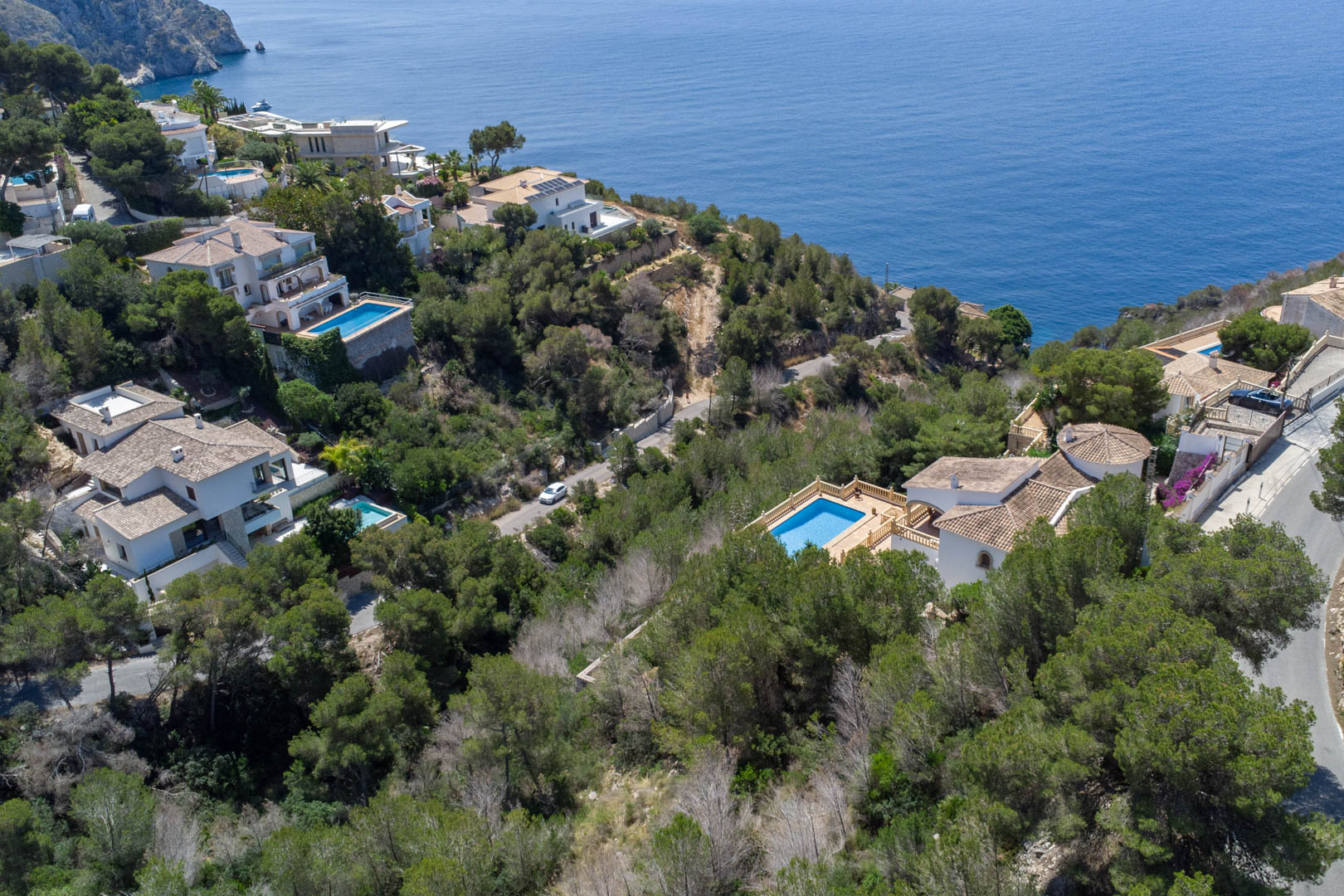 Vista aérea de parcelas residenciales en Costa Nova, Jávea, rodeadas de pinos mediterráneos con vistas panorámicas al mar y villas con piscina privada.