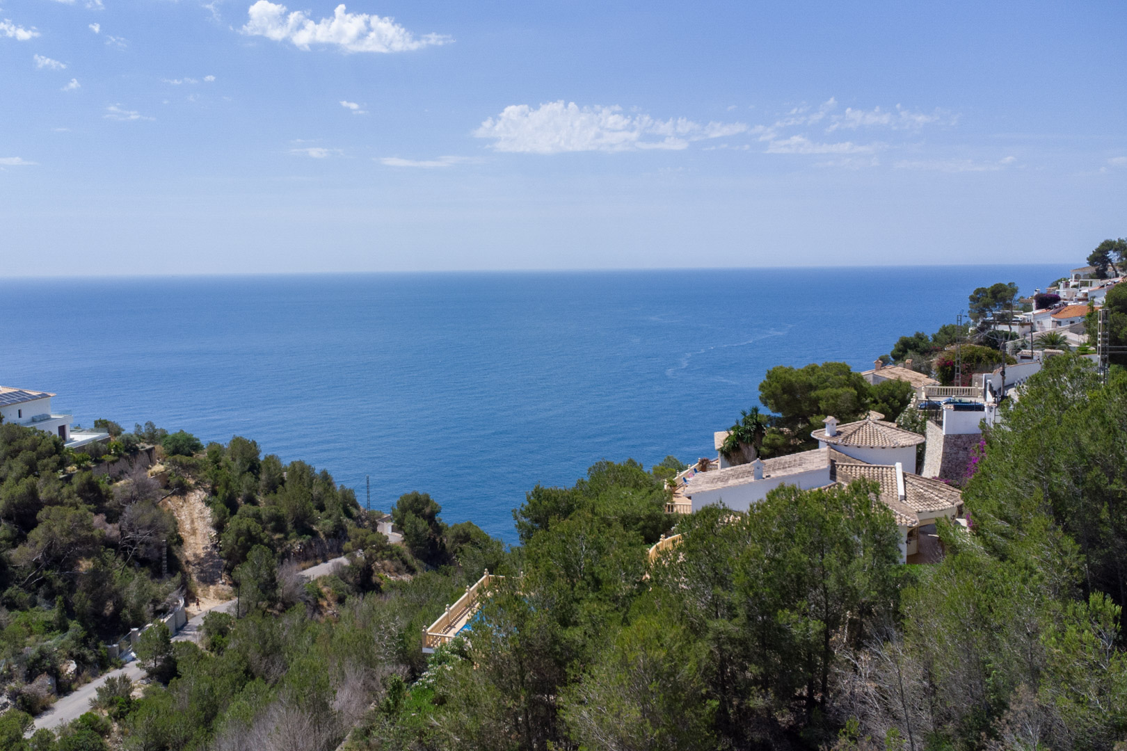 Vista aérea panorámica del mar Mediterráneo desde la costa de Jávea, mostrando la densa vegetación de pinos y villas tradicionales con tejados de terracota.