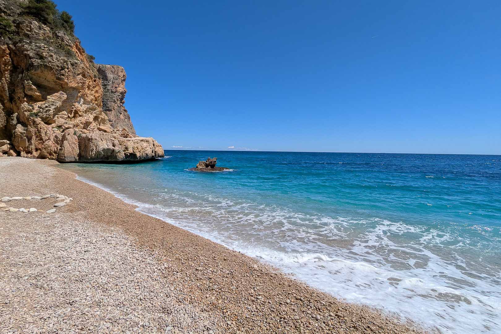 Cala Llebeig, una cala virgen de grava y aguas cristalinas flanqueada por acantilados, accesible directamente desde la zona de La Arnella en Moraira.