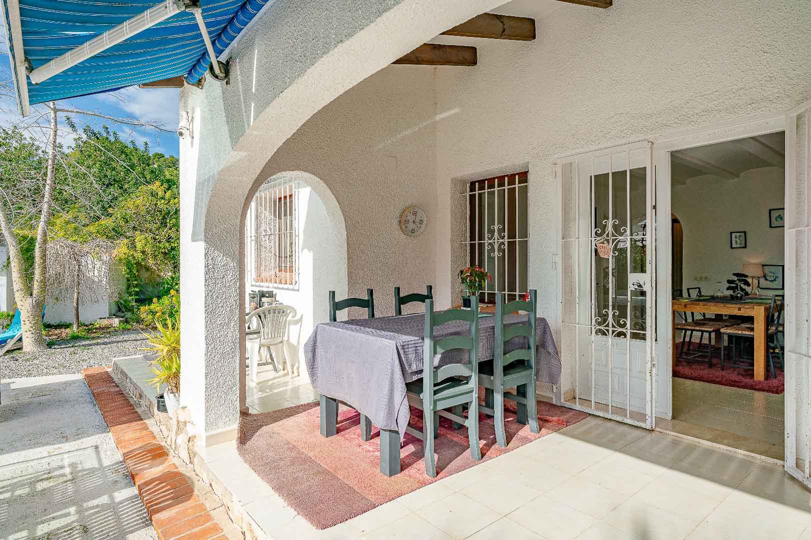 Porche cubierto con arcos de estilo mediterráneo, vigas de madera y comedor exterior. La zona conecta el jardín con el interior a través de puertas con rejas de seguridad.
