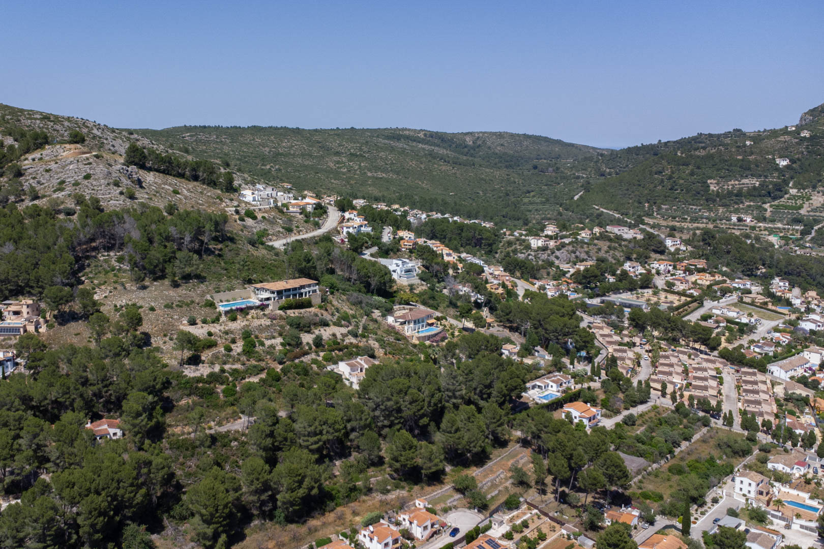 Vista aérea panorámica del Residencial Vall de Pop en Alcalalí, mostrando la integración de las villas en la ladera del valle rodeadas de vegetación mediterránea.