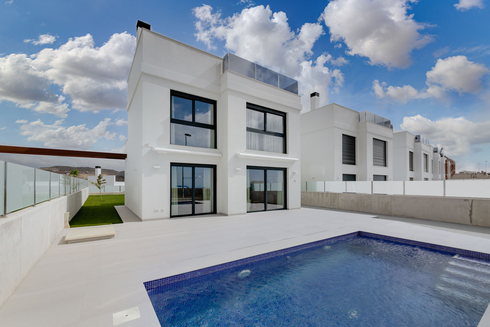 Fachada contemporánea blanca con carpintería negra, amplia terraza de gres porcelánico y piscina privada de gresite azul.
