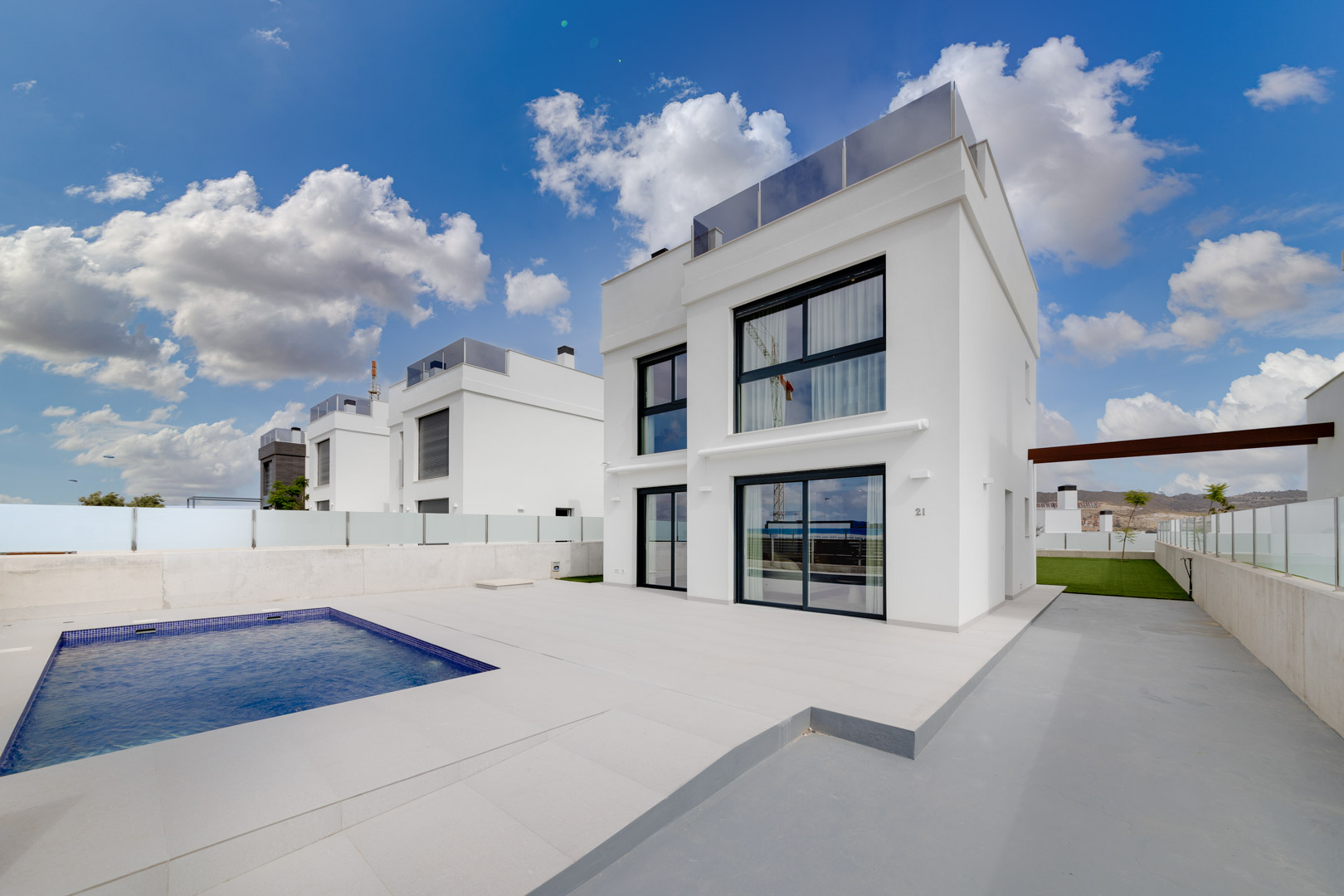 Fachada contemporánea de color blanco con grandes ventanales, terraza pavimentada y piscina privada rectangular bajo un cielo despejado.