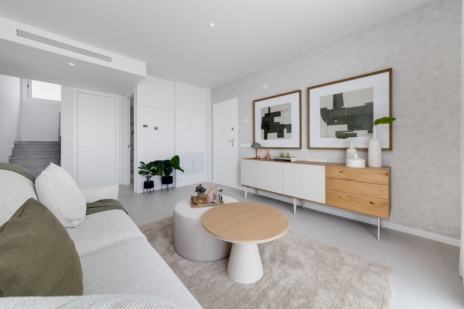 Salón contemporáneo con mobiliario de líneas limpias, aparador de madera y blanco, y zona de estar con sofá de tonos neutros y mesa de centro circular.