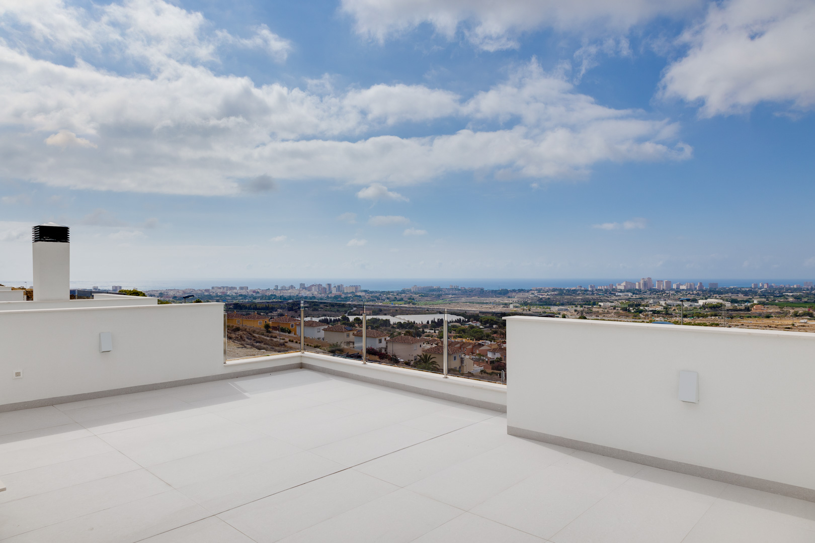 Terraza superior con pavimentos cerámicos de gran formato, barandillas de cristal y vistas panorámicas despejadas hacia la costa y el mar Mediterráneo.